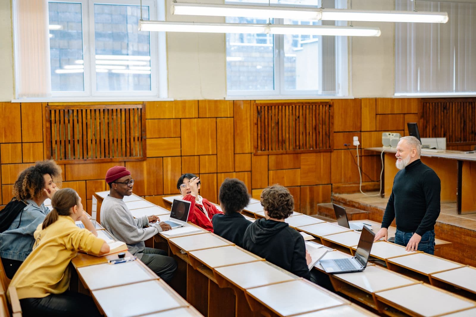 Instructor taking questions from adult learners in a college lecture room, laptops open on the desks.