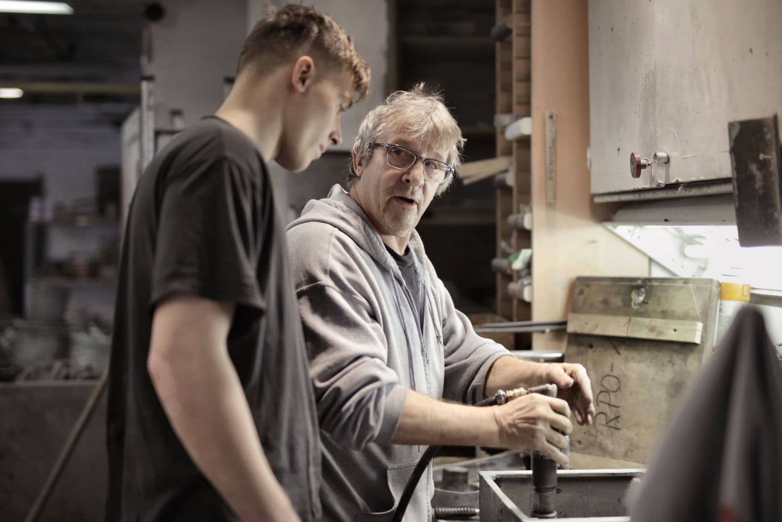 Instructor walking a learner through a machine check at a workshop bench.
